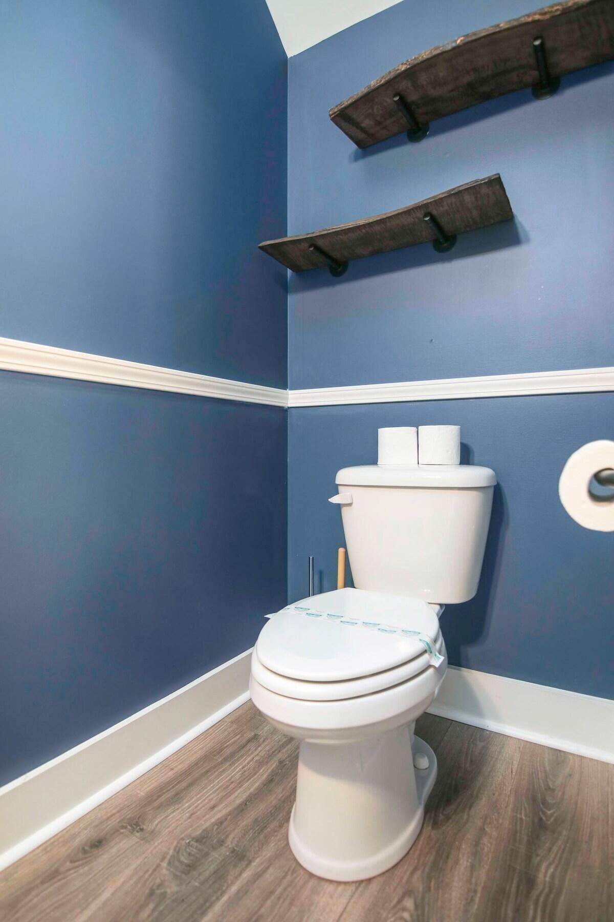 Une salle de bain avec des toilettes blanches, des murs bleus et un plancher en bois.