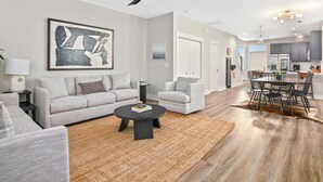 A modern living room with a grey sofa, a coffee table, and a dining area with a wooden table and chairs.