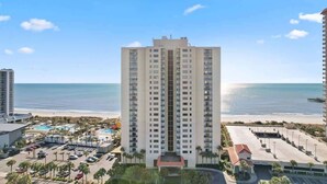 A high-rise hotel with a central courtyard, a pool area, and a view of the beach. - Oceanfront condo with balcony & resort pool (Myrtle Beach)