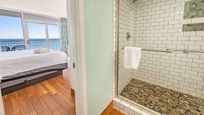 A room with a bed, a glass shower enclosure, and a view of the ocean. - Oceanfront condo with pool & hot tub (Myrtle Beach)