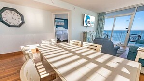 A hotel room with a large dining table, a bed, a TV, and a balcony with a view of the sea. - Oceanfront condo with pool & hot tub (Myrtle Beach)