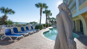 A poolside area with lounge chairs, a statue, and a building with balconies. - Oceanfront condo with pool & hot tub (Myrtle Beach)