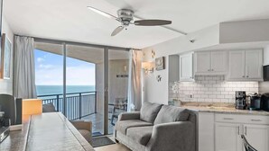 Eine moderne Küche mit weißen Schränken, ein Essbereich mit grauem Sofa und Blick auf den Ozean durch eine Schiebeglastür.