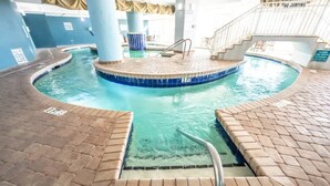 Una piscina interior con un jacuzzi central, rodeada por un solárium de ladrillo y una zona de piscina con azulejos.