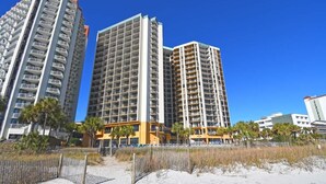 A beachfront hotel with multiple high-rise buildings, a sandy beach, and a wooden fence. - New Coastal Charm, Direct Oceanfront Views, Pools! (Myrtle Beach)