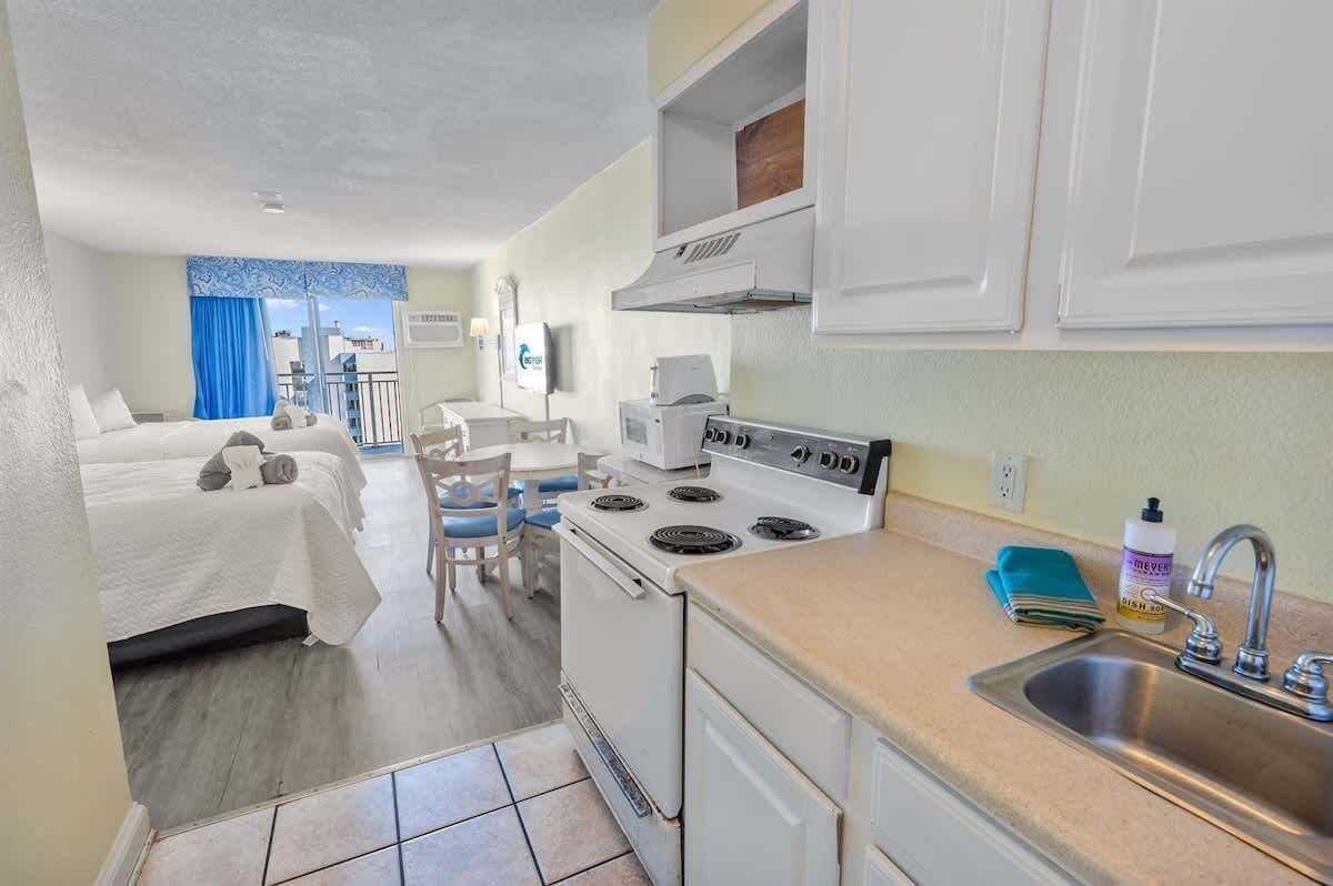 Habitación de hotel compacta con kitchenette, cama con cortina azul y vistas a la ciudad.