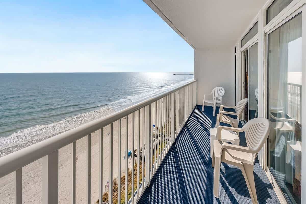 Un balcon avec vue sur l’océan, doté d’une balustrade et de deux chaises en plastique blanches.