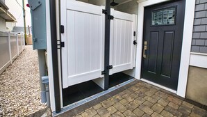 A gated entrance with a black door and a white door, a metal gate, and a gravel pathway leading to a brick-paved area.