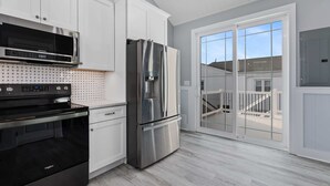 A modern kitchen with stainless steel appliances, white cabinetry, and a large sliding glass door leading to a balcony.