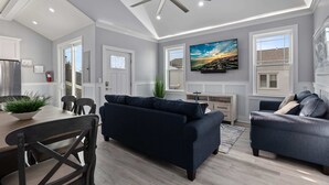A modern living room with a dark blue sofa, a dining table with chairs, a ceiling fan, and a painting on the wall.