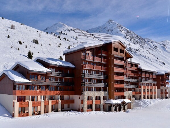 A multi-story hotel with balconies, set against a snowy mountain backdrop.