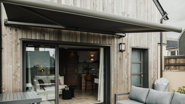 Patio esterno moderno con porta scorrevole in vetro che dà su una zona pranzo, un divano grigio e un tavolino.