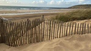 Una spiaggia con una recinzione di legno e dune.
