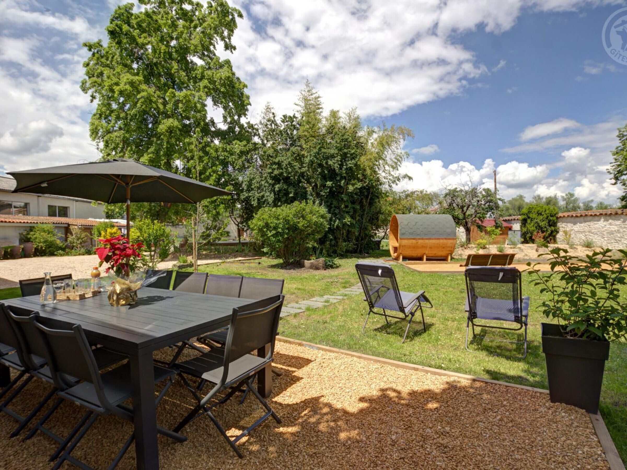 A patio area with a table and chairs, surrounded by trees and a wooden barrel.
