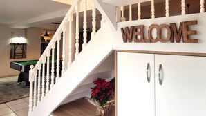 A staircase with a white railing leading to a room with a 'WELCOME' sign above a cabinet.