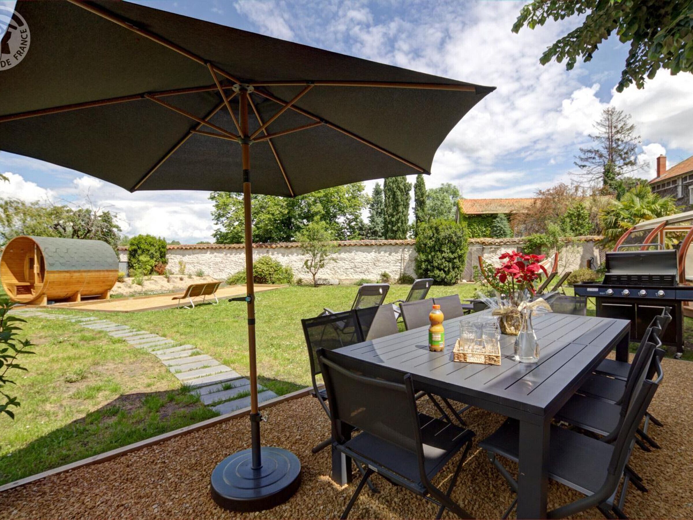 Un espace extérieur aménagé en terrasse, avec une table et des chaises, un grand parasol et un barbecue.