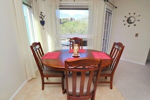 Un comedor con mesa y sillas de madera, un jarrón como centro de mesa y vistas por la ventana.