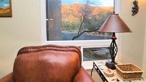 A room with a leather chair, a lamp, a basket, and a window with a view of a desert landscape. - CV 8245  Cozy Condo at the Base of the Mountains (Tucson)