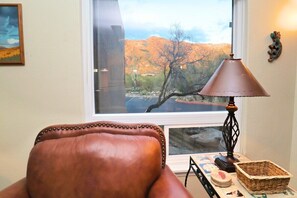 A room with a leather chair, a lamp, a basket, and a window with a view of a desert landscape. - CV 8245  Cozy Condo at the Base of the Mountains (Tucson)