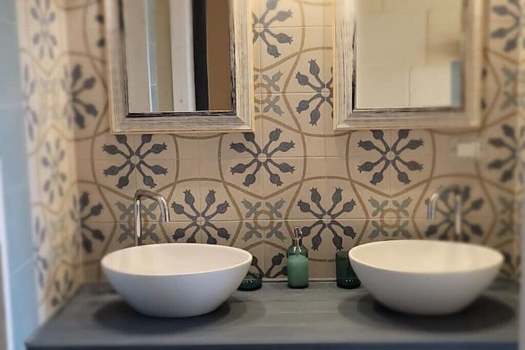 Ein Badezimmer mit zwei großen weißen Waschbecken, jeweils einem Spiegel darüber und wandförmigem Musterfliesen.