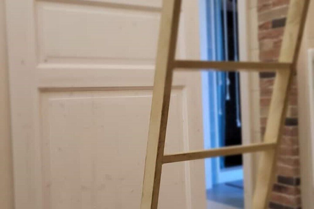 Eine Holzleiter lehnt an einer weißen Tür.