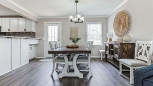 A modern kitchen with white cabinets, a wooden dining table, and a chandelier. - Charming 3BR Farmhouse • Fenced Acre • Madison (Madison)