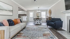 A modern living room with a sofa, a coffee table, a fireplace, and a dining area in the background. - Charming 3BR Farmhouse • Fenced Acre • Madison (Madison)
