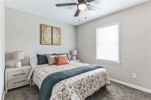 A bedroom with a bed, nightstands, a ceiling fan, artwork on the wall, and a window. - Charming 3BR Farmhouse • Fenced Acre • Madison (Madison)