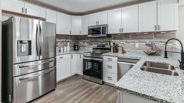 A modern kitchen with stainless steel appliances, white cabinetry, granite countertops, and a built-in oven. - Charming 3BR Farmhouse • Fenced Acre • Madison (Madison)