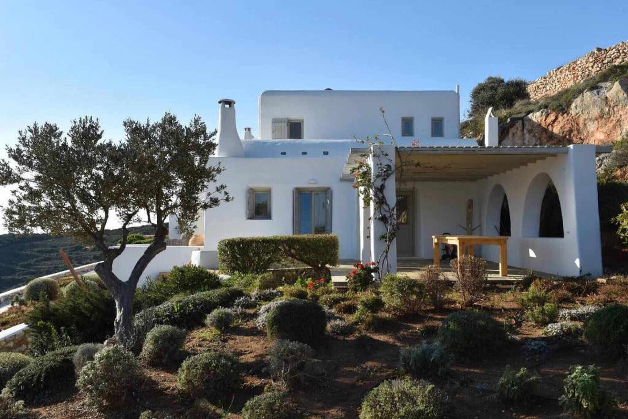 Um edifício branco com telhado plano, janelas em arco e um pequeno pátio com mesa e cadeiras.