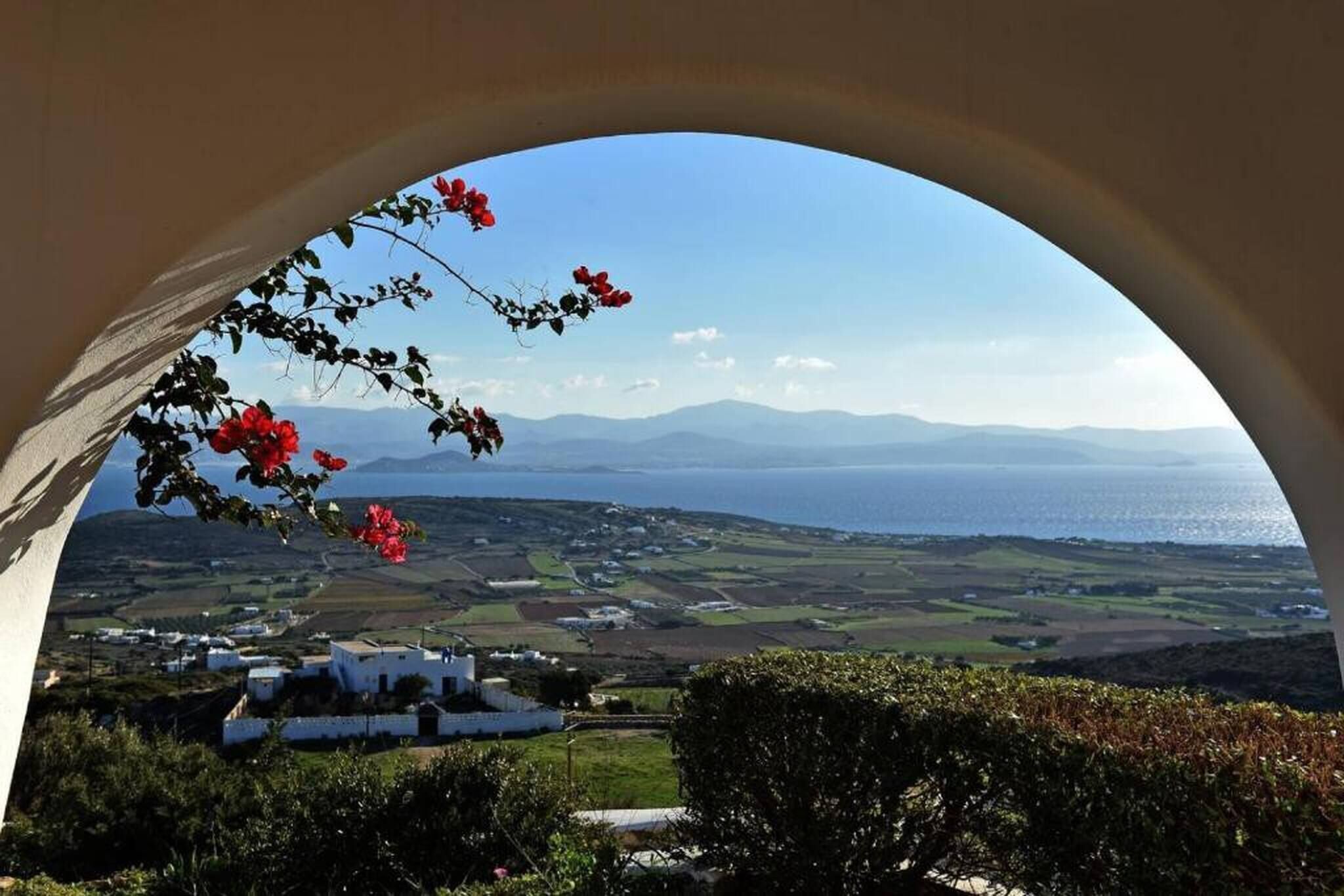 A view through an archway with a landscape of fields, a body of water, and distant mountains.