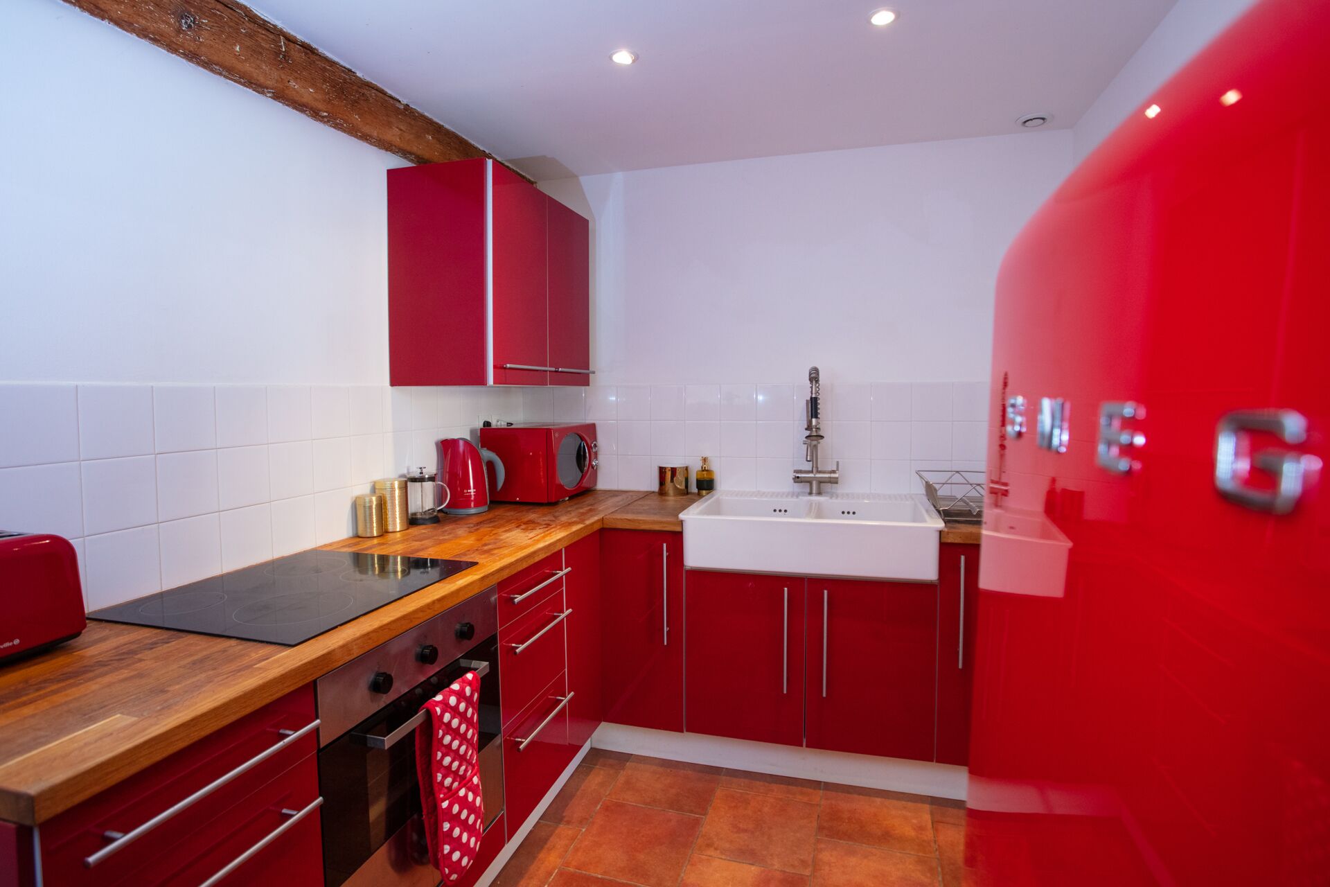 A compact kitchen with red cabinets, a black stovetop, and a white sink.