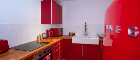 A compact kitchen with red cabinets, a black stovetop, and a white sink.