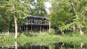 A lakeside cabin with a deck and a covered porch, surrounded by trees and a calm body of water. - Hot Tub, Fire Pit, Secluded, 5 Minutes Eureka (Eureka Springs)