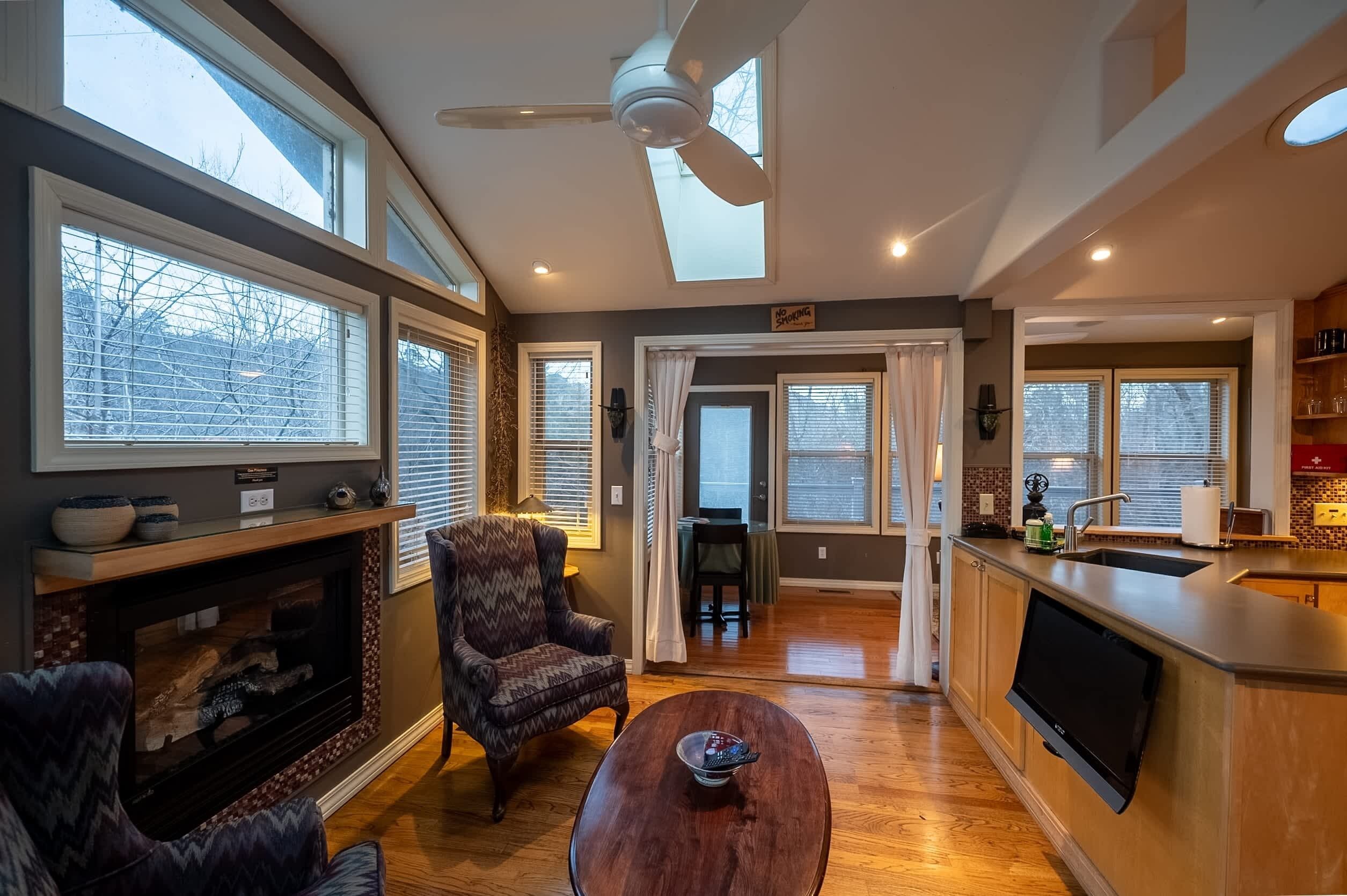A spacious living room with a fireplace, comfortable seating, a large TV, and a kitchen area with a sink and counter.