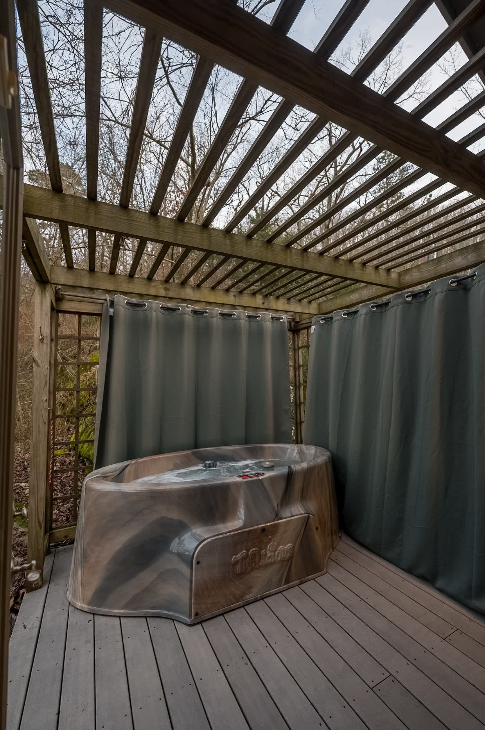 Ein Whirlpool unter einer Holzpergola mit Blick auf kahle Bäume.