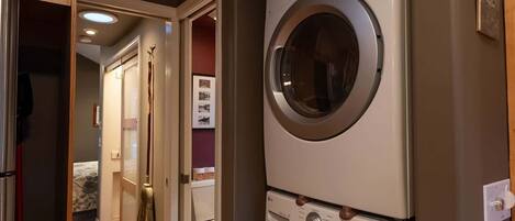 A laundry room with two stacked front-loading washers and dryers, wooden flooring, and a visible fire extinguisher.