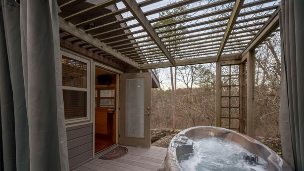 A hot tub under a pergola, a wooden door, and a view of the surrounding area. - Hot Tub, Fire Pit, Secluded, 5 Minutes Eureka (Eureka Springs)