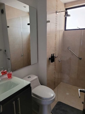 Ein Badezimmer mit Toilette, Waschbecken, Spiegel, Dusche und einem Fenster.
