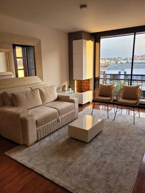 Ein modernes Wohnzimmer mit einer Couch, Sesseln, einem Couchtisch und einem großen Fenster mit Blick auf die Stadt.