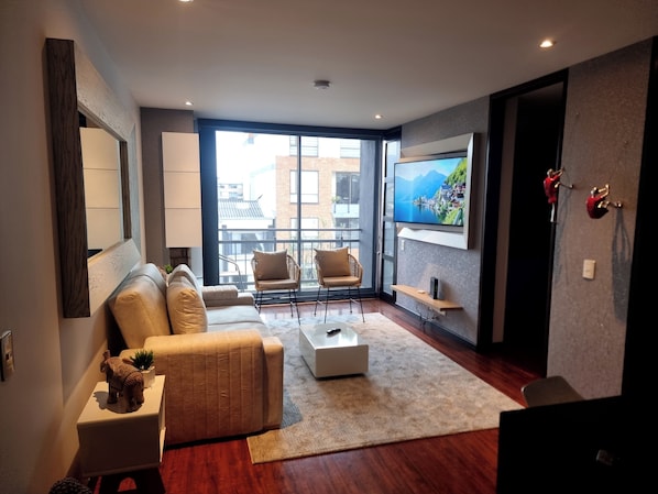 Ein modernes Wohnzimmer mit einer Couch, Sesseln, einem Couchtisch, einem Fernseher und einem großen Fenster.