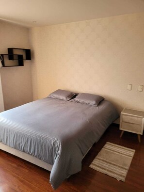 Un dormitorio con cama, mesita de noche, estante en la pared y alfombra.