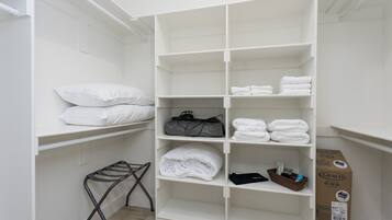 A white closet with shelves containing folded towels, a black bag, and a Graco pack n play playard.