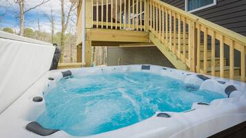 A hot tub on a wooden deck with a staircase leading to a house.