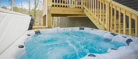 A hot tub on a wooden deck with a staircase leading to a house.