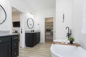 A modern bathroom with a freestanding bathtub, a vanity with a mirror, and a walk-in closet. - Ridgeline Retreat, Your Gateway to NWA Adventure! (Bella Vista)