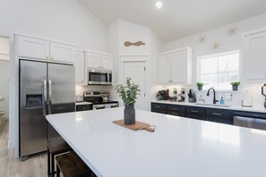 A modern kitchen with white cabinetry, stainless steel appliances, and a central island with a plant. - Ridgeline Retreat, Your Gateway to NWA Adventure! (Bella Vista)