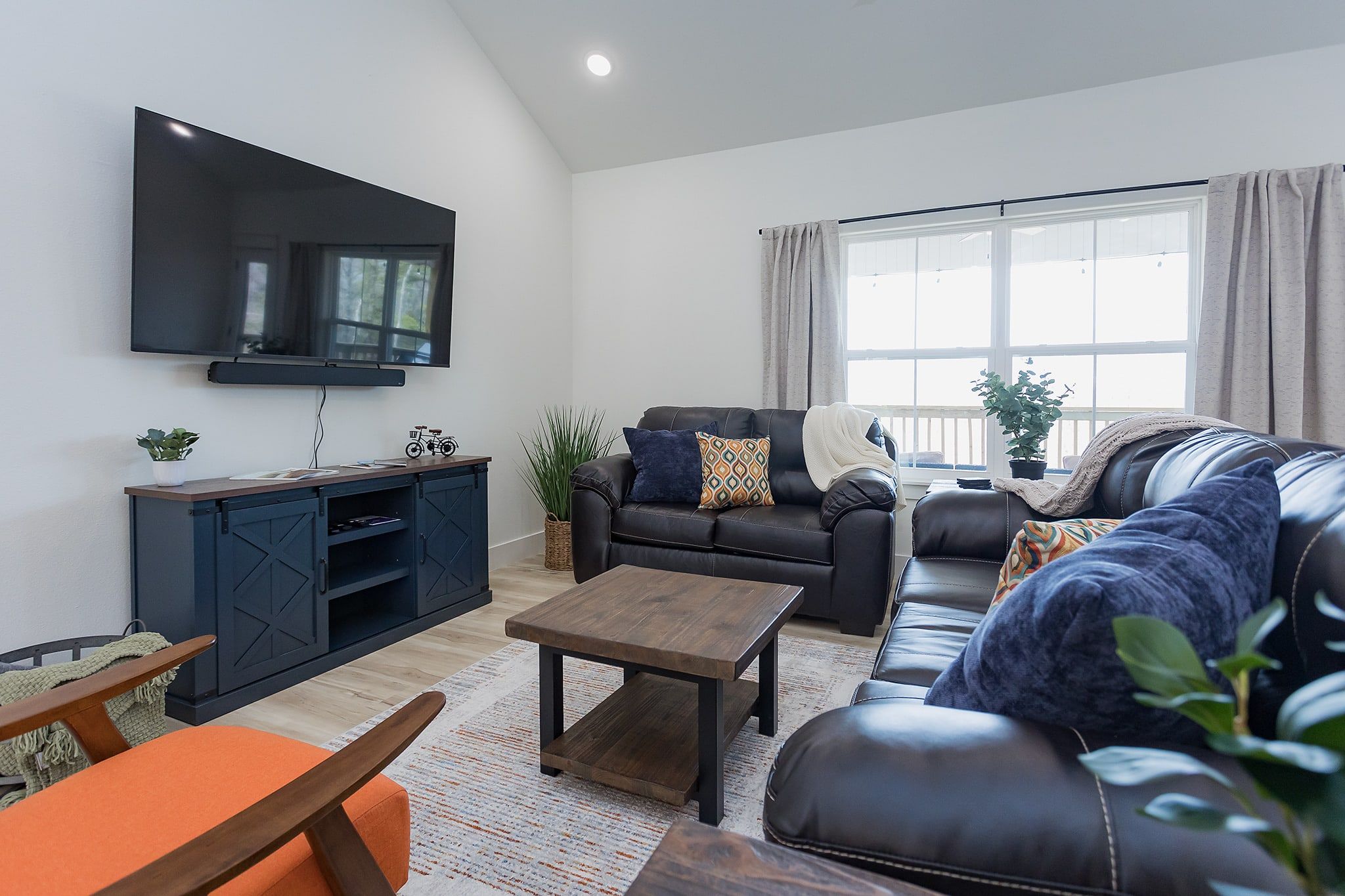 Een moderne woonkamer met een flatscreen televisie, een leren bank, een houten salontafel en een groot raam met gordijnen.