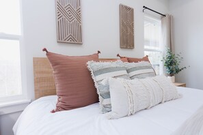 A neatly made bed with a wooden headboard, two decorative pillows, and a small bedside table with a plant. - Ridgeline Retreat, Your Gateway to NWA Adventure! (Bella Vista)