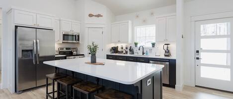 Una cocina moderna con una isla central, electrodomésticos de acero inoxidable y una zona de asientos con taburetes de bar.